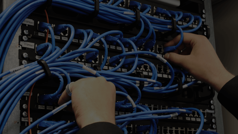 Technician's hands meticulously connecting blue network cables into a professional server rack, demonstrating expert cabling installation.